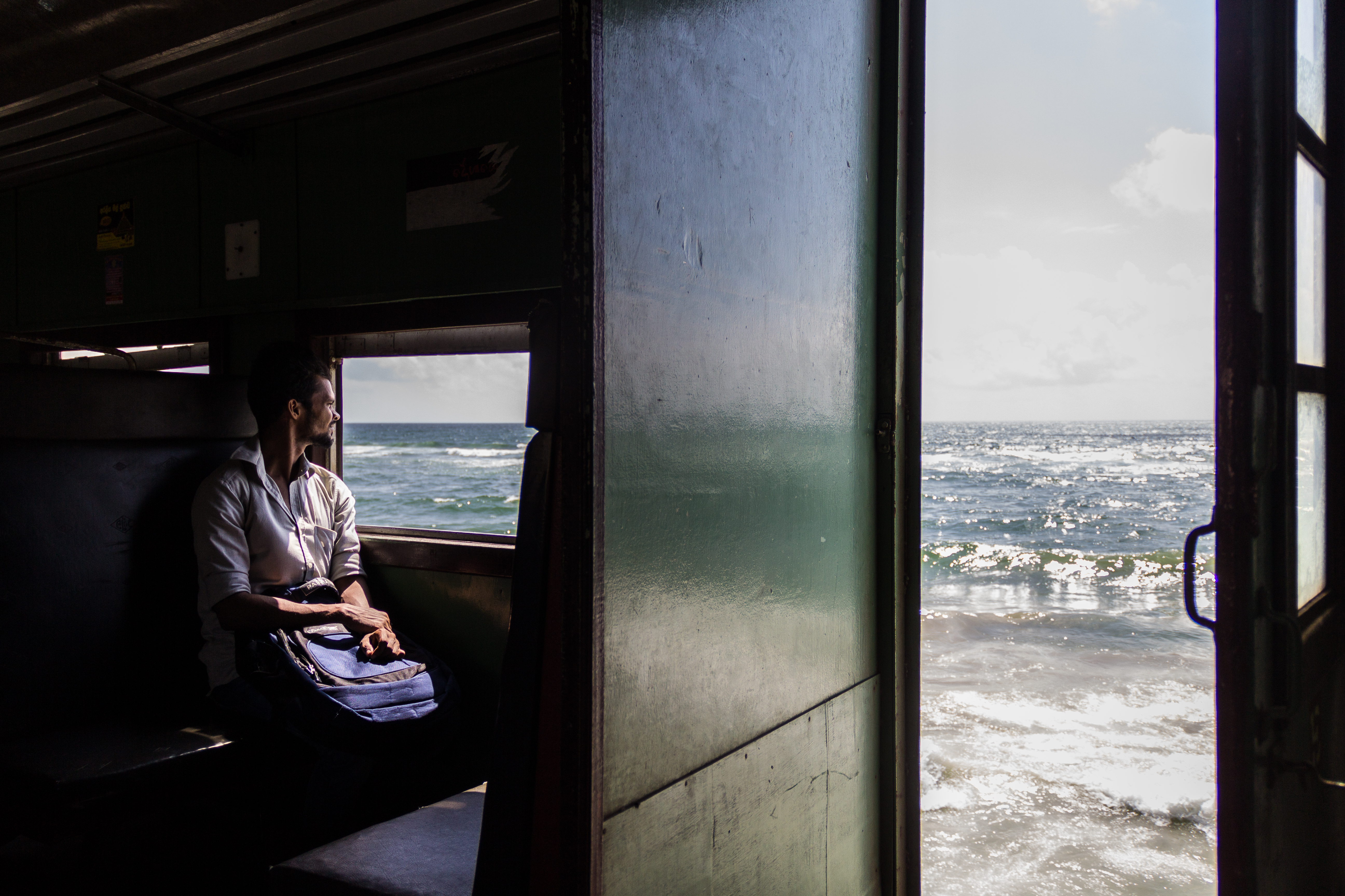Portret van man die door het raam staart naar de zee in de trein in Sri Lanka door fotograaf Lucie Bataillie